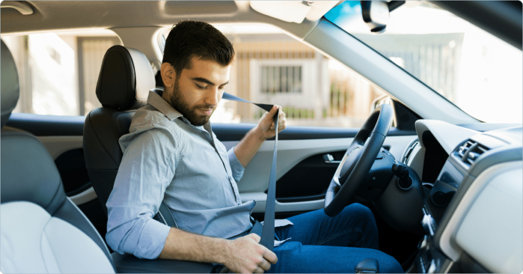 A man sitting in the driver's seat of a car, fastening his seatbelt.